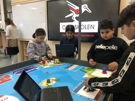 Børn koder robotter foran skærm med Odinskolens logo